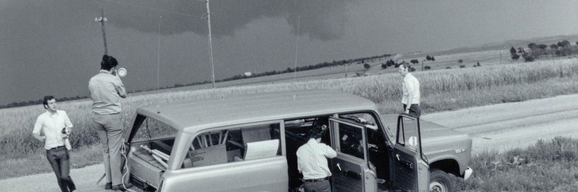 vintage black and white photo of people around a vehicle with equipment with storm clouds in the background